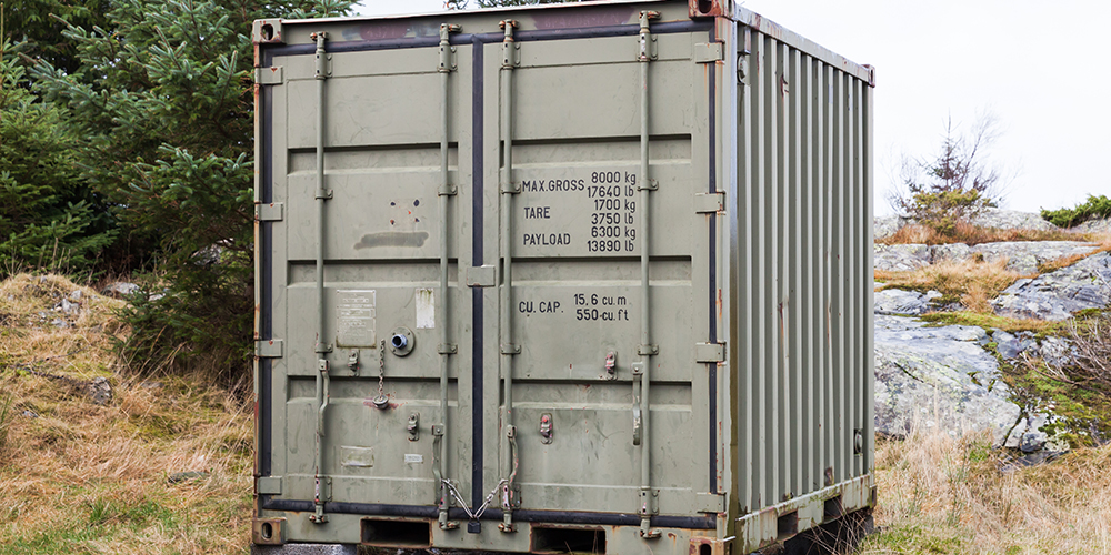 Military green cargo container stands on grass, industrial shipping equipment